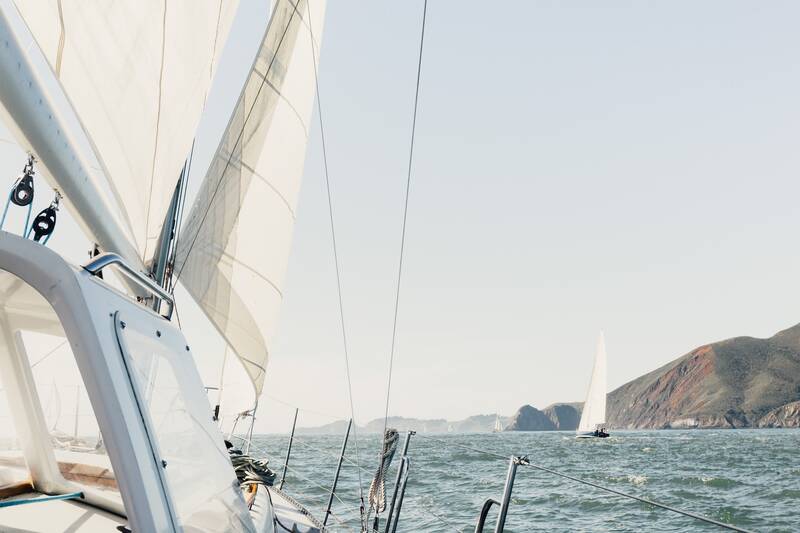 Segelboot auf dem Wasser mit einem weiteren Segelboot und einer hügeligen Küste im Hintergrund