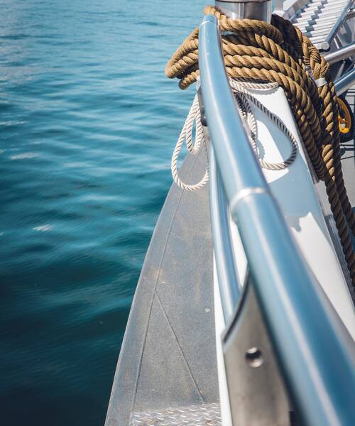 Aufgerollte Festmacherleinen an Deck neben einer Edelstahlreling auf einem Boot.
